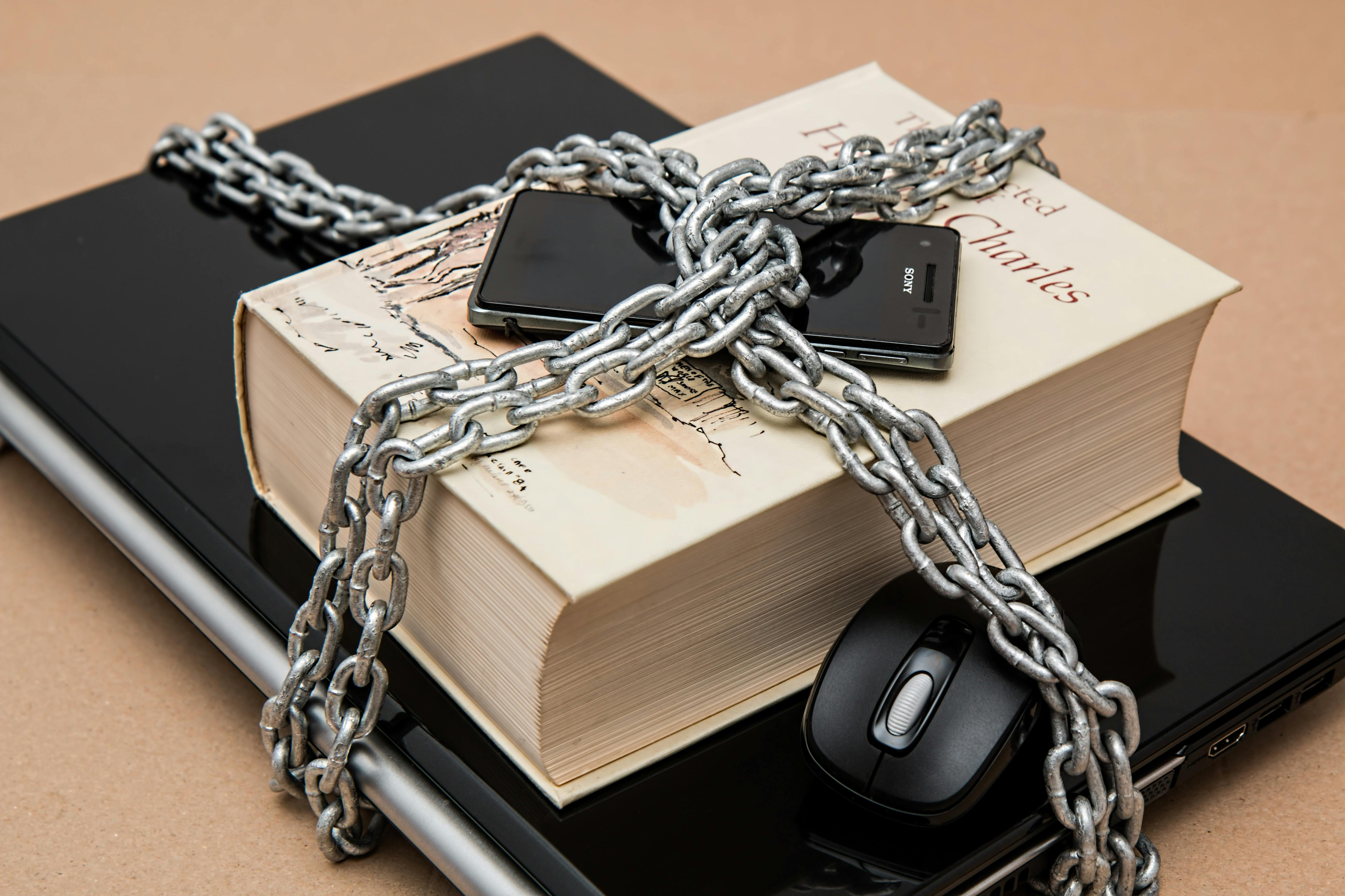 mobile phone on top of a thick book on top of a laptop wrapped and locked down in a steel chain
