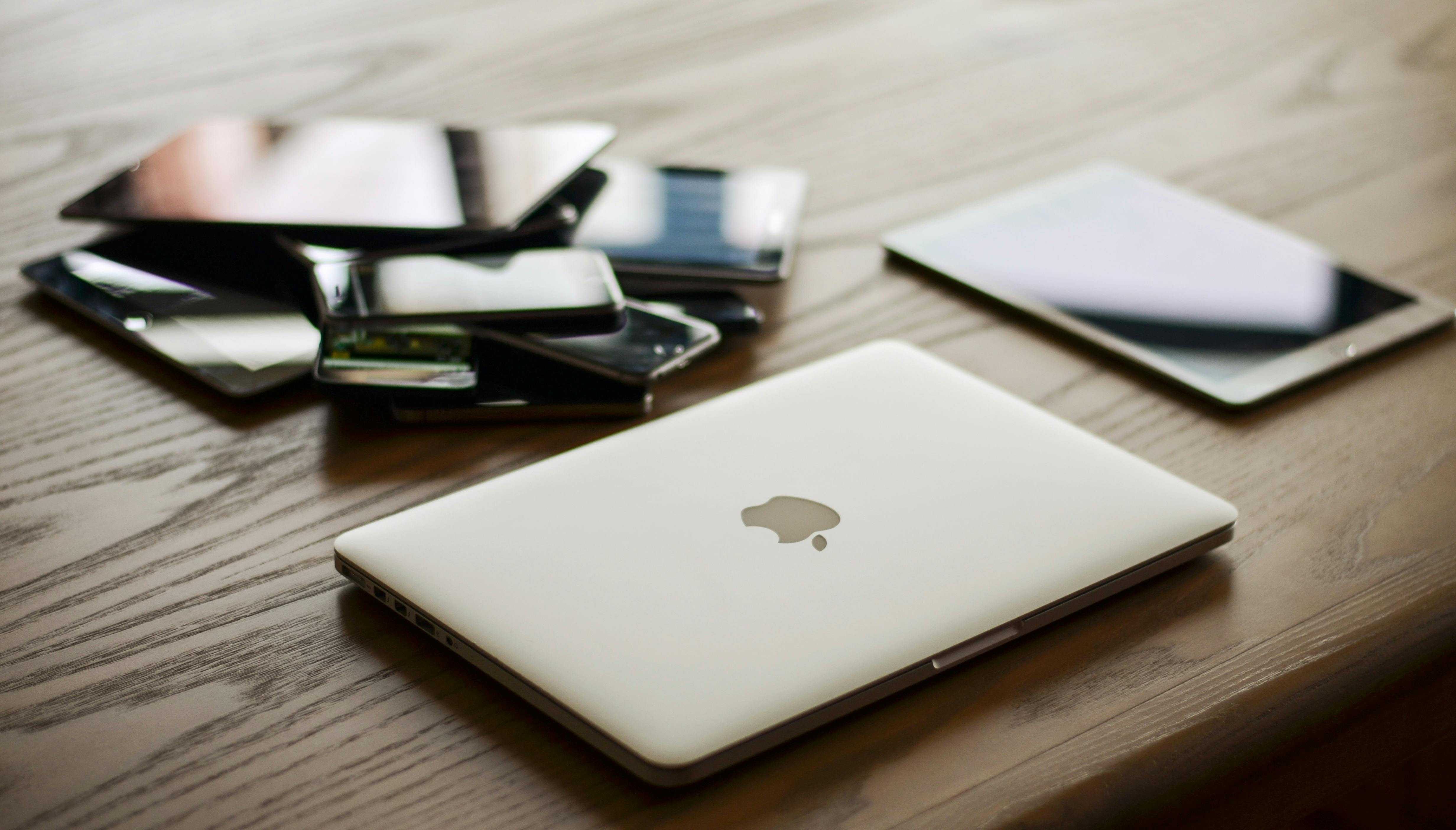 pile of phones on a desk beside a MAC and tablet